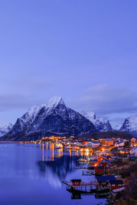 Illuminated buildings by sea against sky at dusk