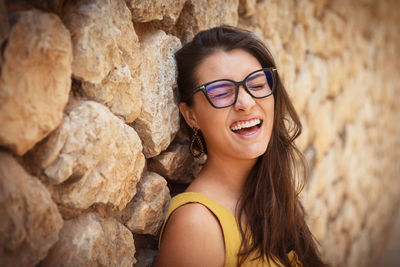 Young woman standing in front of a stone wall. wearing glasses making a funny face at the camera