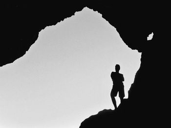 Low angle view of silhouette man standing on rock against sky