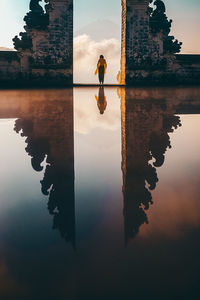 Reflection of woman amidst built structure on lake against sky