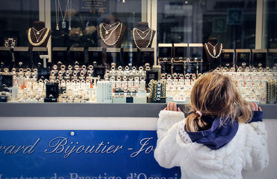 Rear view of girl looking at jewelry on retail display