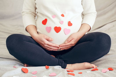 Midsection of woman holding heart shape while sitting on bed at home