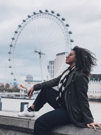 Woman sitting on retaining wall against london eye