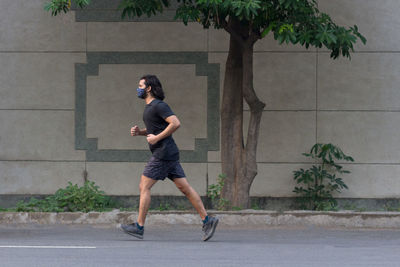 Side view of a man wearing a mask jogging on the road.