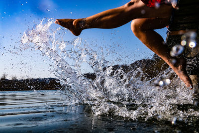 Low section of woman splashing water at lake