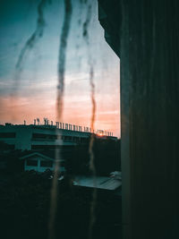 Silhouette bridge by buildings against sky at sunset