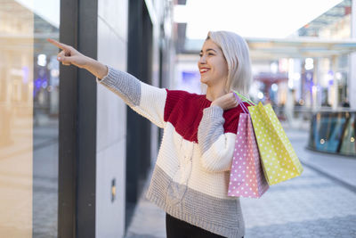 Portrait of young woman holding shopping bags while standing in city