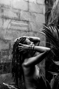 Side view of naked woman standing by plant against wall