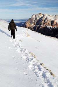 Rear view of hiker walking on snow covered mountain against sky