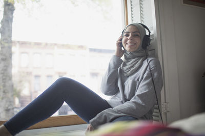 Smiling young woman sitting on window