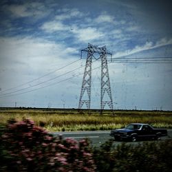 Electricity pylon on field against cloudy sky