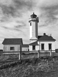 Lighthouse on field by building against sky