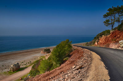 Road by sea against clear blue sky