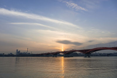 Bridge over river in city against sky during sunset