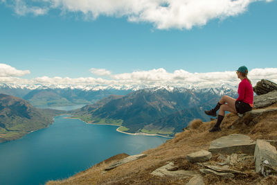 Woman sitting on rock looking at mountains against sky