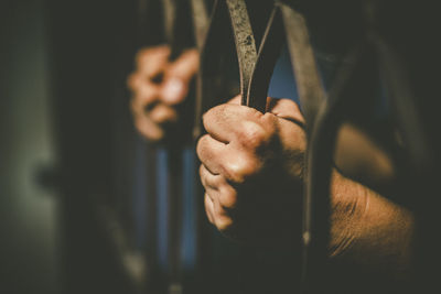 Cropped hands of male prisoner holding prison bars