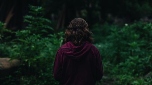 Rear view of woman standing against trees in forest