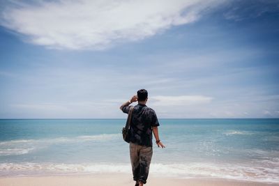 Rear view of man standing on beach against sky