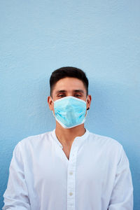 Young latin man with mask on blue background