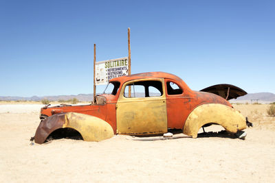 Abandoned car by information sign against clear sky