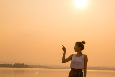 Woman pointing while standing against sea and sky during sunset