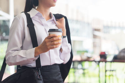 Businesswoman holding disposable cup while standing against building in city