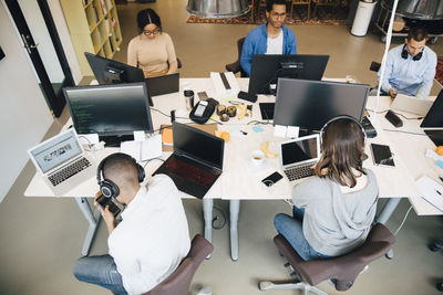 High angle view of it professionals using technology while sitting at desk in creative office