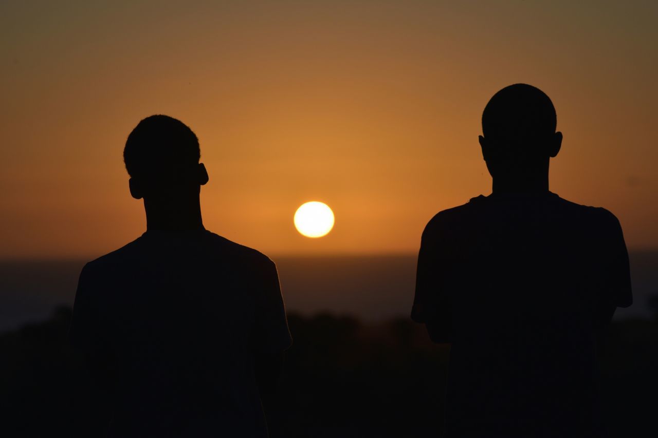 sunset, silhouette, standing, lifestyles, men, leisure activity, sky, orange color, sun, rear view, beauty in nature, scenics, waist up, tranquility, three quarter length, tranquil scene, looking at view, nature