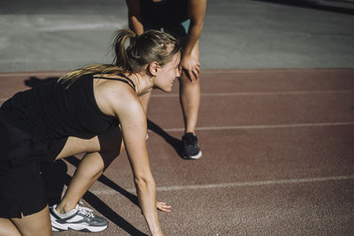 Side view of young woman preparing for sprint on running track