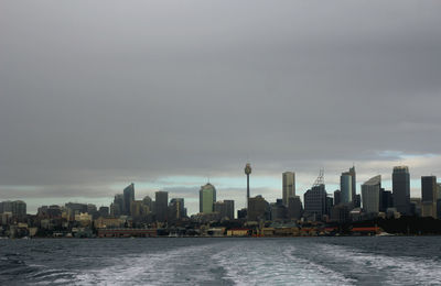 Cityscape by sea against cloudy sky