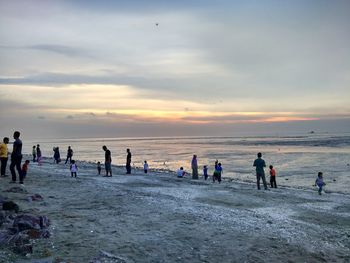 People on beach against sky during sunset