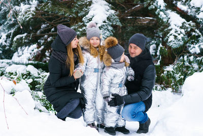 Mom with dad and son and daughter in winter in yard near snow-covered christmas