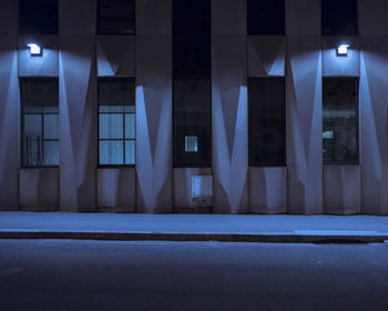 Empty road by illuminated building at night