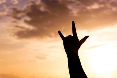 Silhouette hand gesturing against sky during sunset