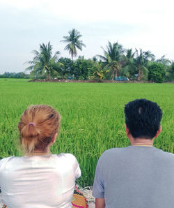 Rear view of man and woman sitting against field