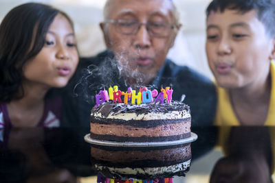 Grandparents and grandchildren blowing birthday candles on cake at home