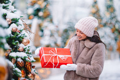Smiling woman holding christmas gift standing outdoors