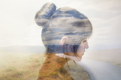 Double exposure of young woman and country road amidst grassy field