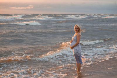 Pregnant woman standing at beach against sky