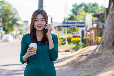 Portrait of young woman drinking coffee while standing in city