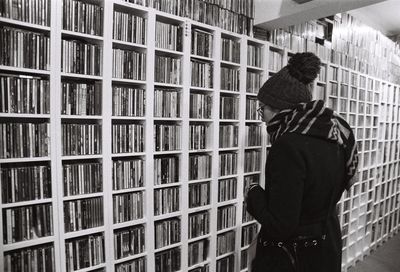 Woman standing by shelves with books in library