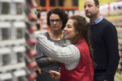 Side view of smiling saleswoman assisting mature couple in hardware store