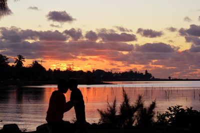 Silhouette people by lake against sky during sunset