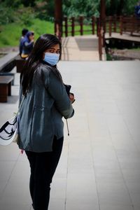 Full length of woman with mobile phone walking on footpath