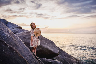 Man standing on rock at sea shore against sky