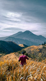 Rear view of man looking at mountains against sky