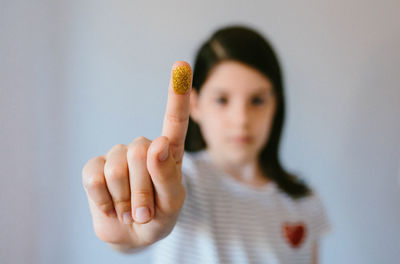 Serious young girl looking at camera while showing her finger covered of golden glitter