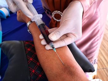 Midsection of doctor removing blood through injection in clinic