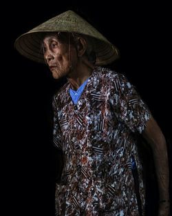 Senior woman wearing conical hat while standing against black background