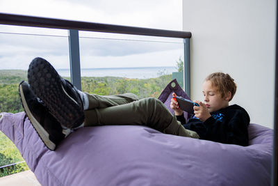 Side view of boy using mobile phone while lying on bed at home